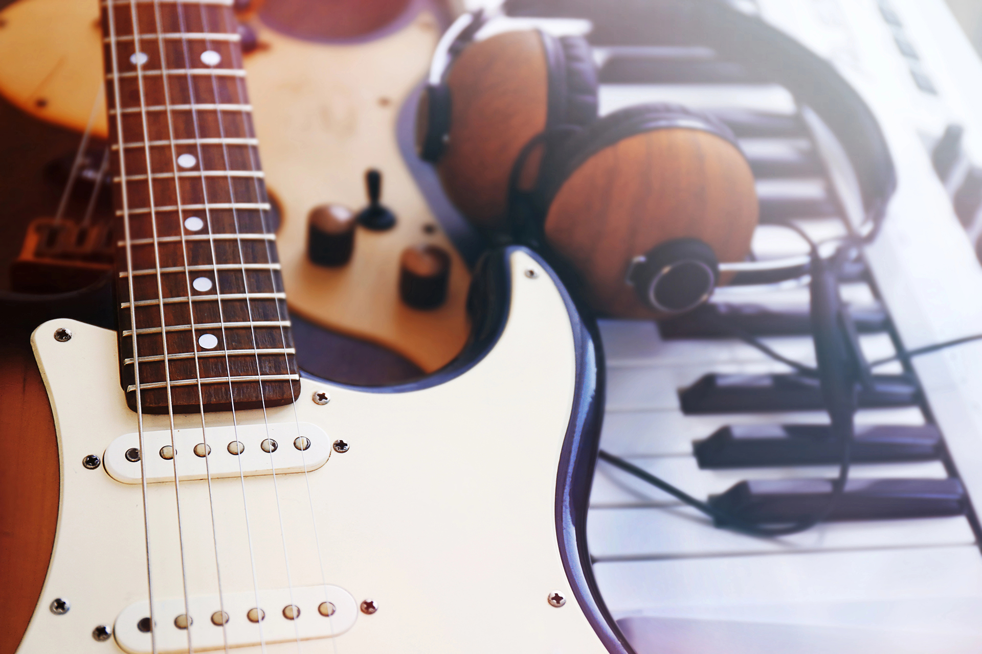 An electric and a classic guitar on top of a piano, next to a pair of headphones