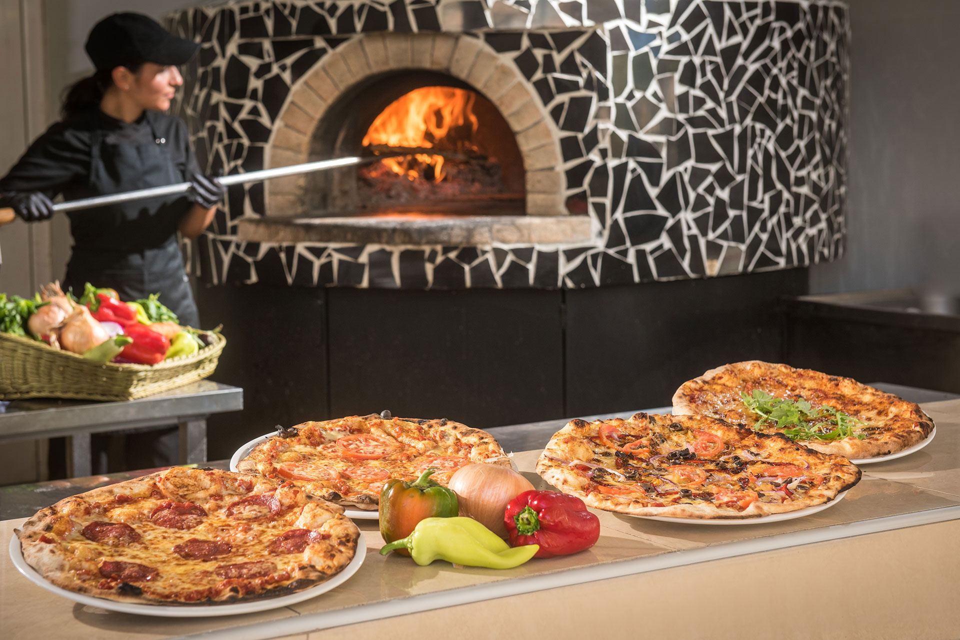 Gouves Park pizzas in display with a cook in the background putting a pizza in the stove